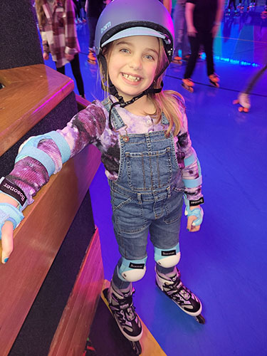 Young girl smiling at an indoor roller rink with people standing together in the background