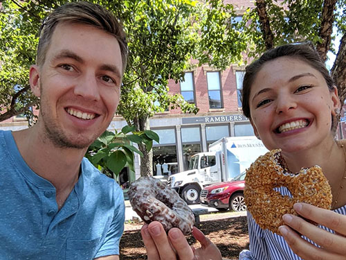 Young man and woman smiling and eating donuts in an urban park