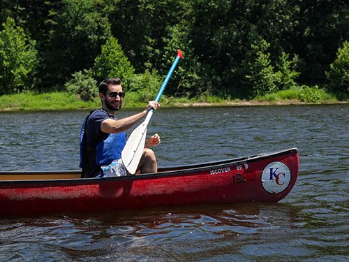 A young man paddling a red canoe