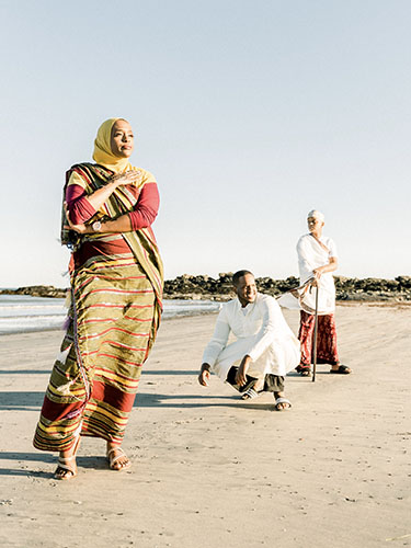 Asha Mohamud standing on the sand at the beach with two gentleman behind her