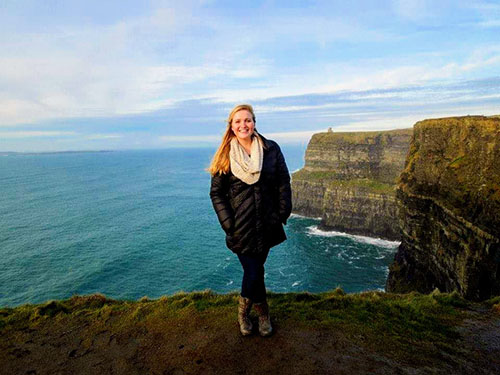 Katelyn Chadwick standing on the edge of a cliff with more cliffs and the ocean behind her