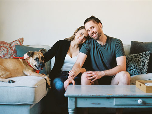 Young woman, man, and dog sitting together cozily on a sofa
