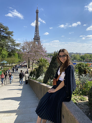 young woman sitting on a stone wall with the Eiffel tower in the backdrop