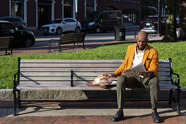 a man sitting on a park bench reading a newspaper
