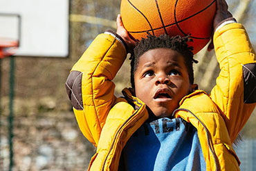 Young boy in yellow jacket shooting a basketball