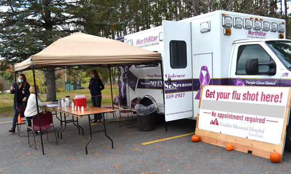 A mobile health vehicle and staff are shown in a parking lot offering drive up flu shots