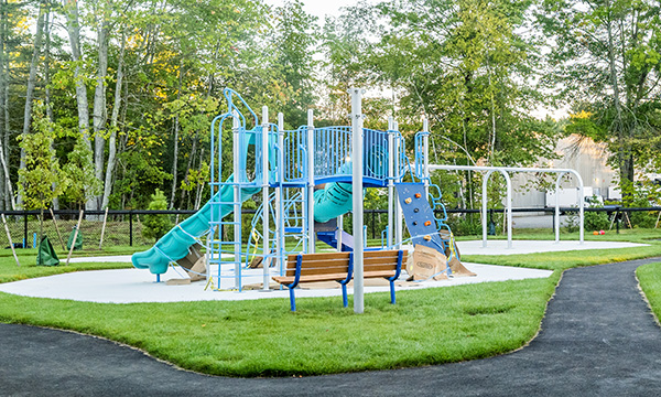 playground with a slide, climbing ladders, and swings outside in a park setting next to a bench