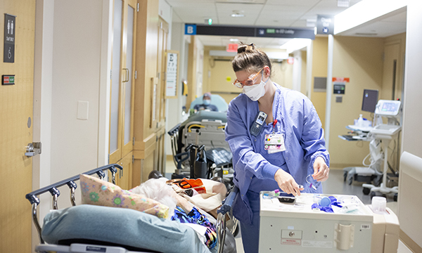 Nurse wearing PPE standing next to a stretcher in an emergency department hallway.