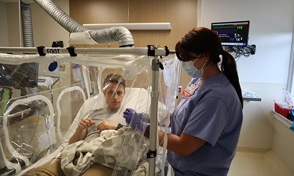 care provider utilizing a Collapsible Aerosolized Particle Enclosure (CAPE) on a bed-bound patient