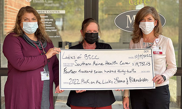 three women wearing masks and holding and over-sized check to benefit SMHC
