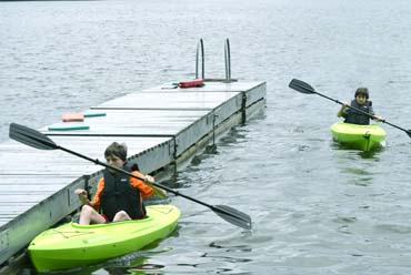 Two young boys in kayaks by a dock