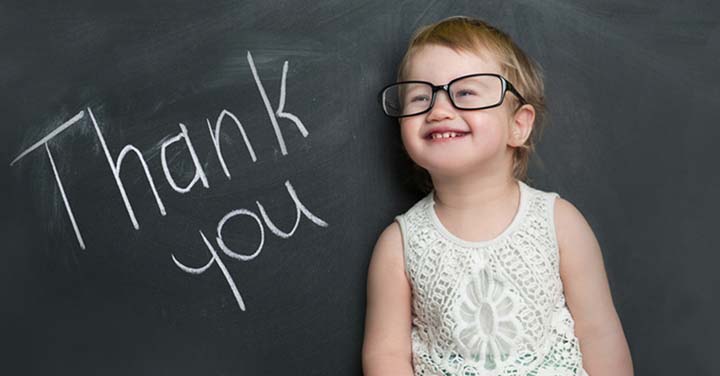 Young girl wearing glasses in front of a blackboard that says "Thank You"