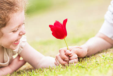 Young girl in the grass holding a bright red flower