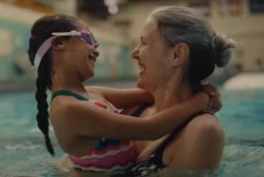 A grandmother smiles while holding her grandchild in an indoor swimming pool