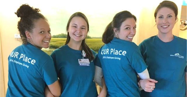 four young women standing together and wearing blue t-shirts that read "our place"